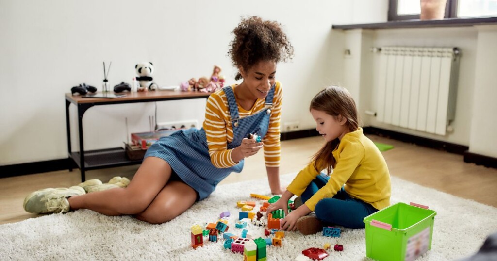 babysitter playing with blocks with little girl on the floor 