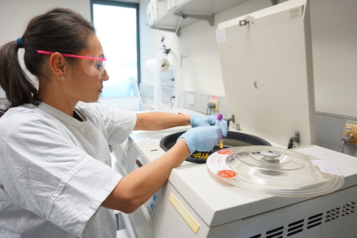 Image of researcher in a laboratory, about to spin some samples in a centrifuge. The researcher is wearing a lab coat and safety glasses.