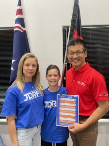 Rebecca and Nikolas Mirco in blue JDRF t-shirts with Sam Lim MP, in a red polo t-shirt holding a JDRF electorate data sheet. 